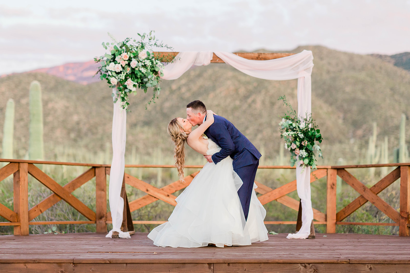 Bride and Groom kissing under the arch with a field of saguaros in the background